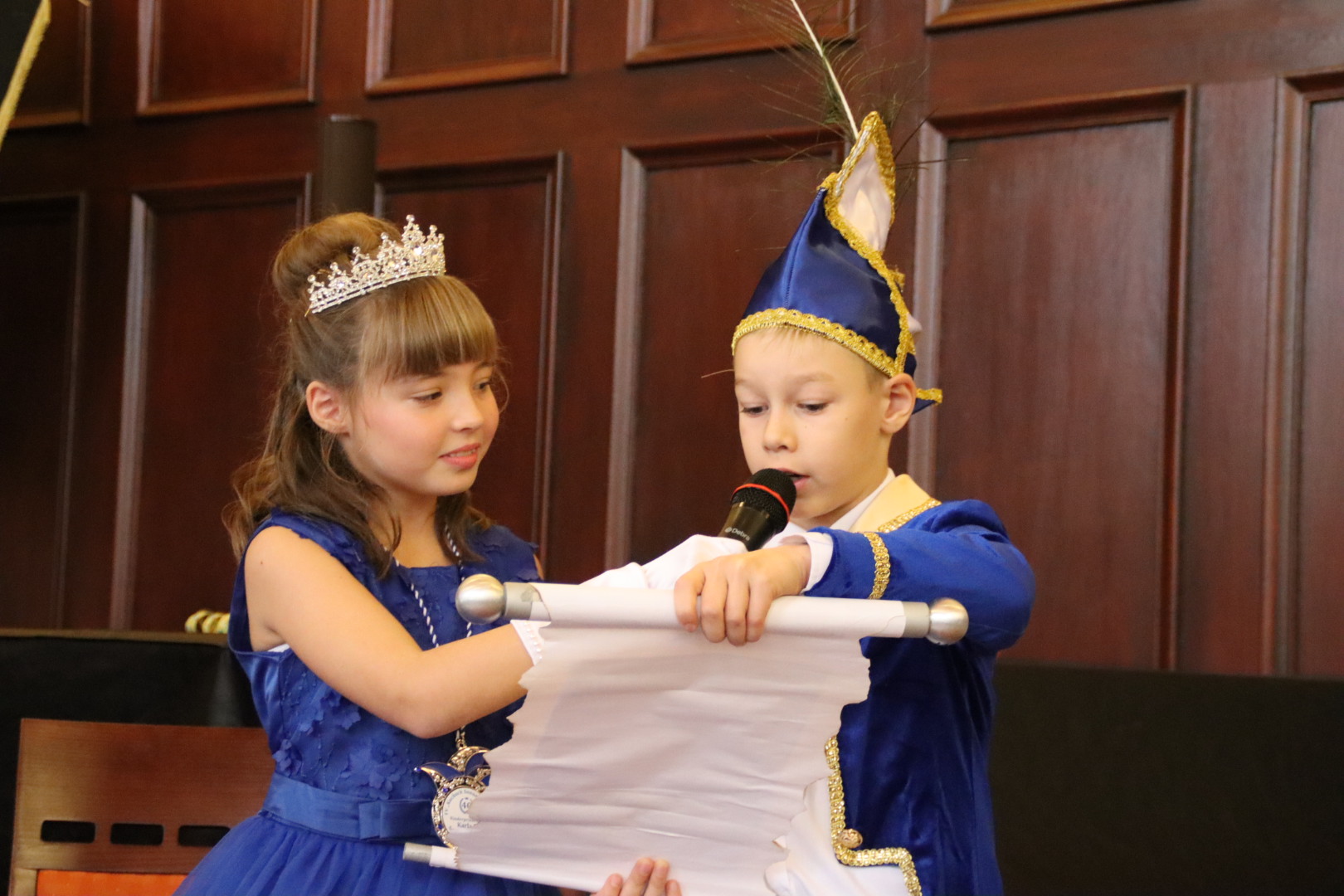 Das Kinder-Prinzenpaar hält eine Schriftrolle und spricht in ein Mikrofon.
