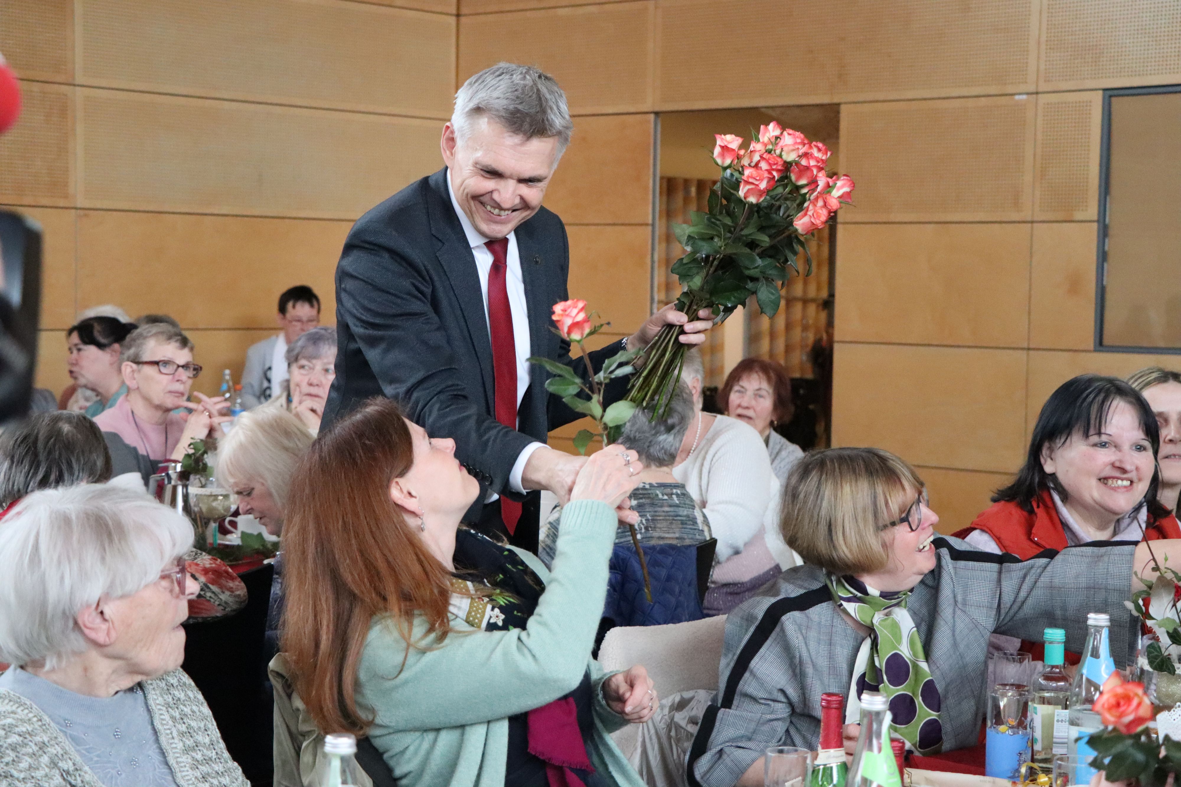 Frauen sitzen an gedeckten Kaffeetischen. Der Bürgermeister Dr. Heiko Voigt verteilt Rosen.