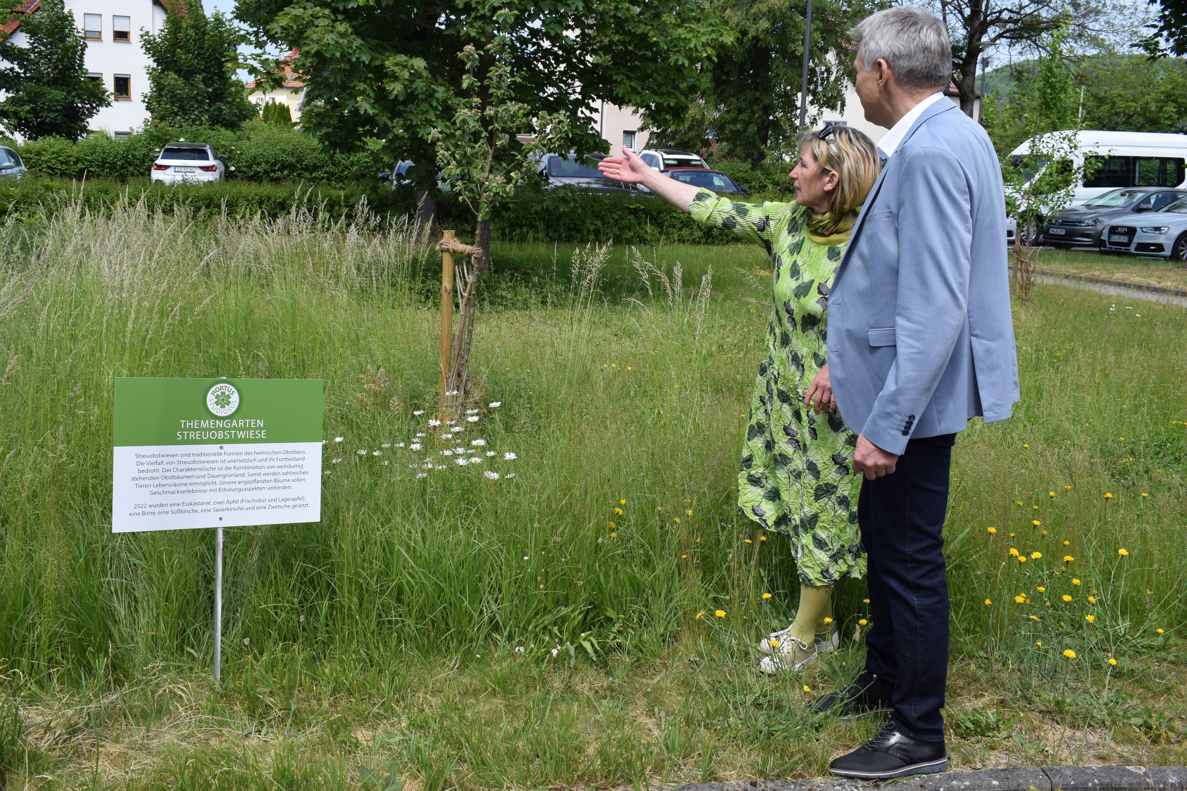 Ein Mann und eine Frau stehen auf einer Wiese. Es ist der Bürgermeister Dr. Heiko Voigt. Dabneben steht ein Schild mit der Aufschrift: Themengarten Streuobstwiese.