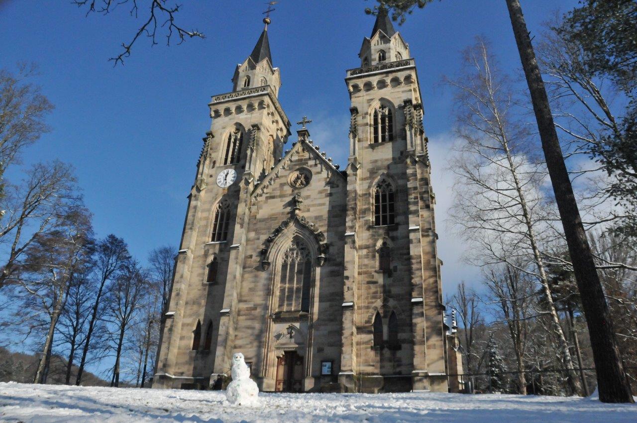 Eine Kirche umgeben von Bäumen. Es liegt Schnee.