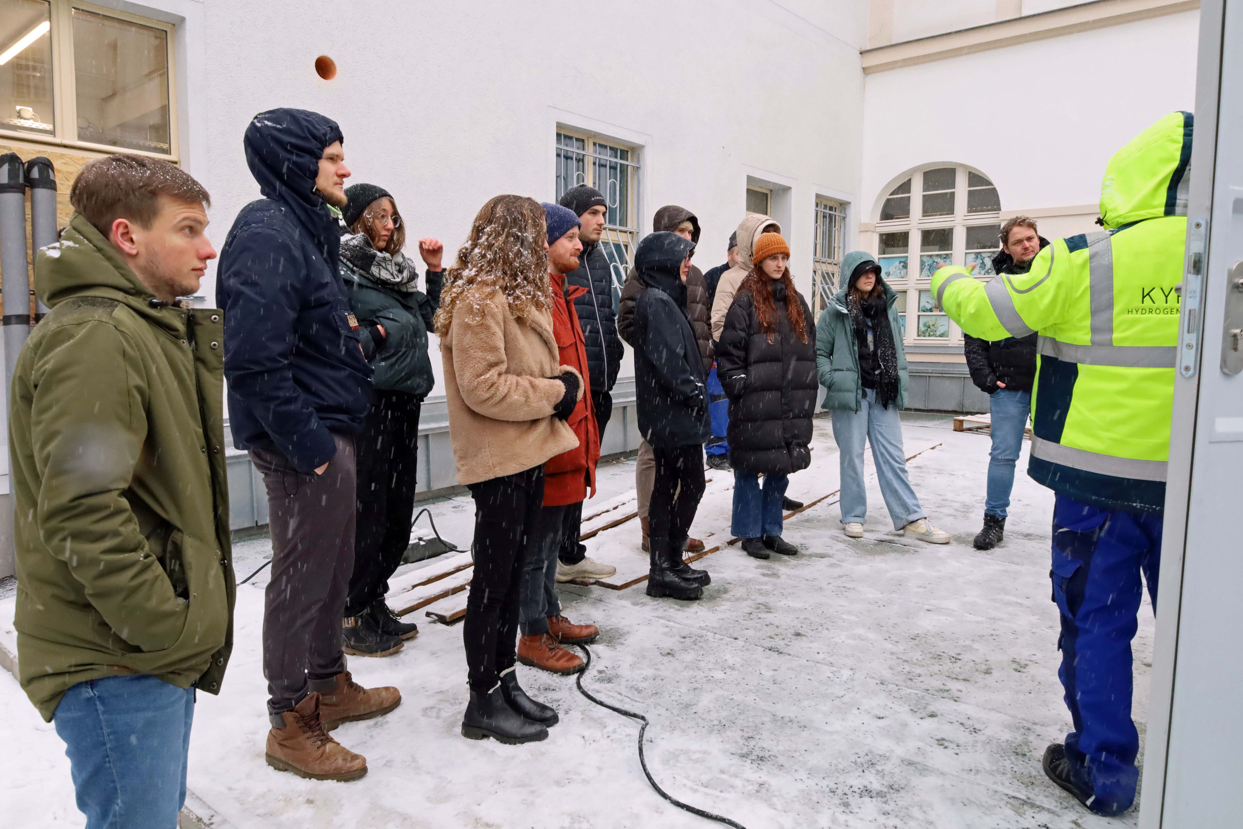 Menschen stehen nebeneinander vor einem Container. Es liegt Schnee.