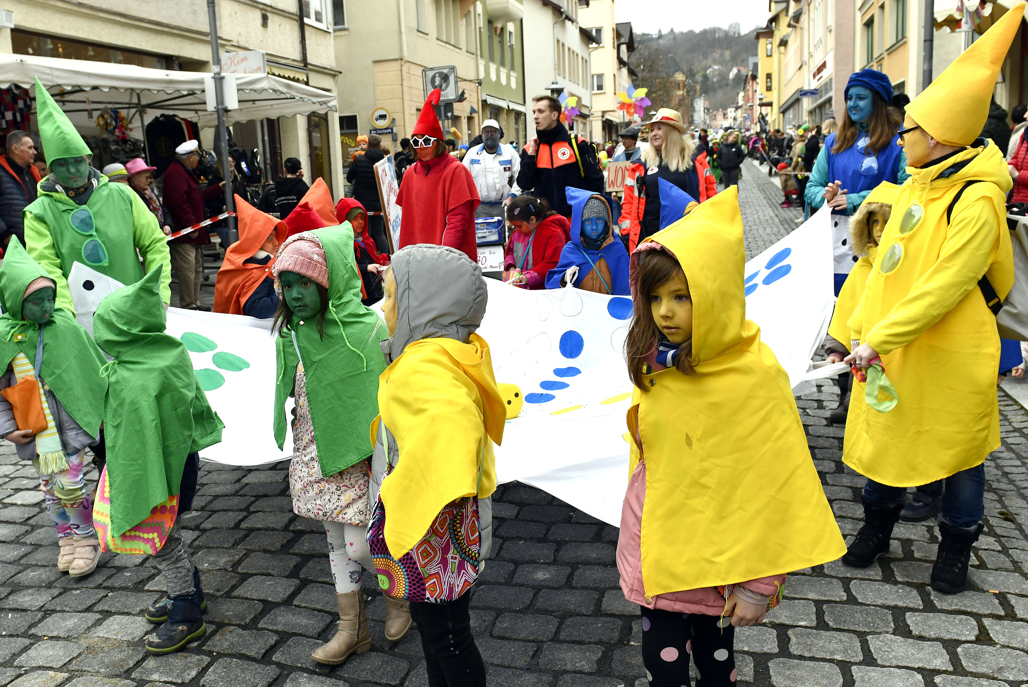 Kinder und Erwachsene sind als Mensch-ärgere-dich-nicht-Figuren gekleidet und tragen ein zugehöriges Spielbrett.