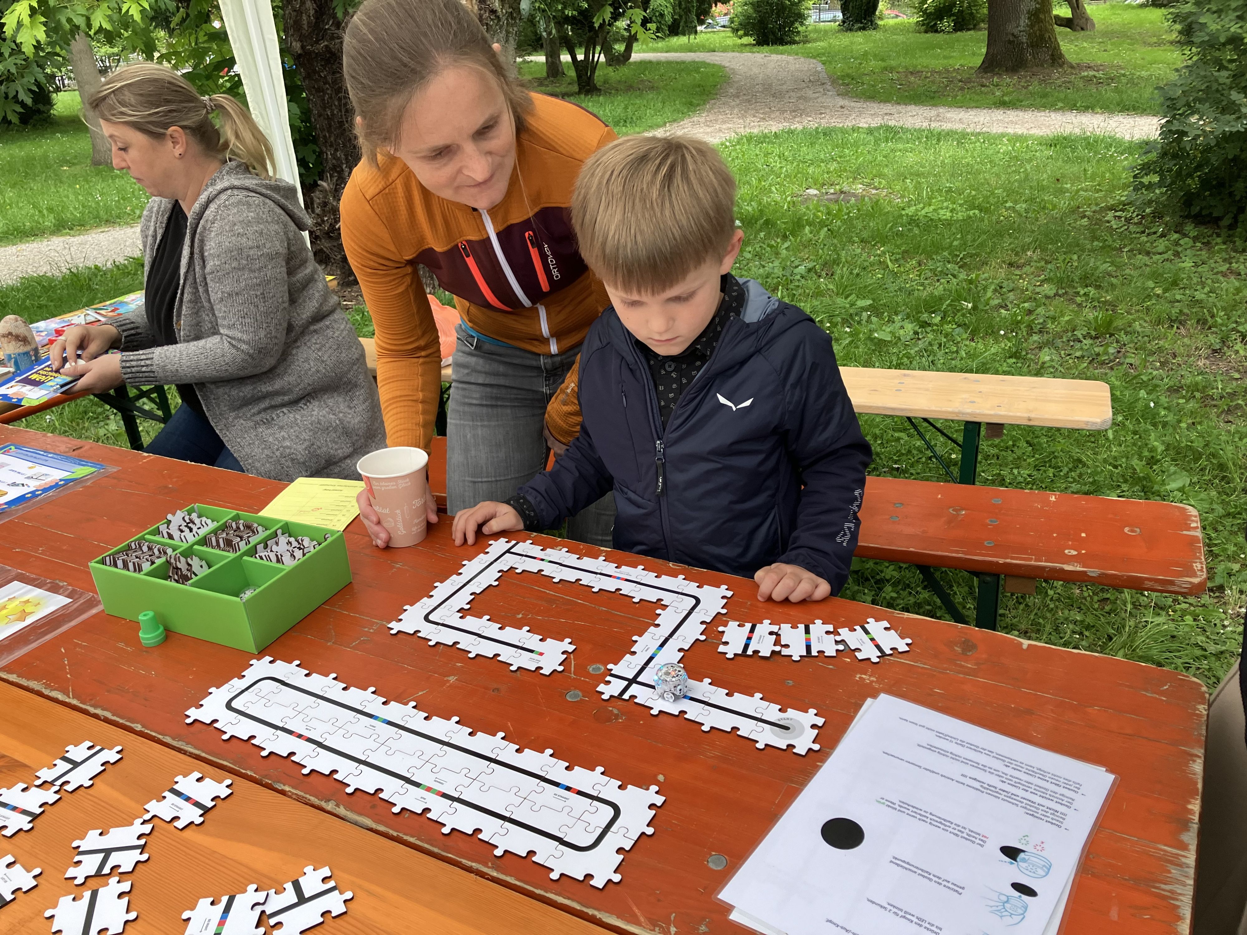 Ein Junge steht vor einem Puzzle mit einer schwarzen Linie. Darauf fährt ein Miniroboter.