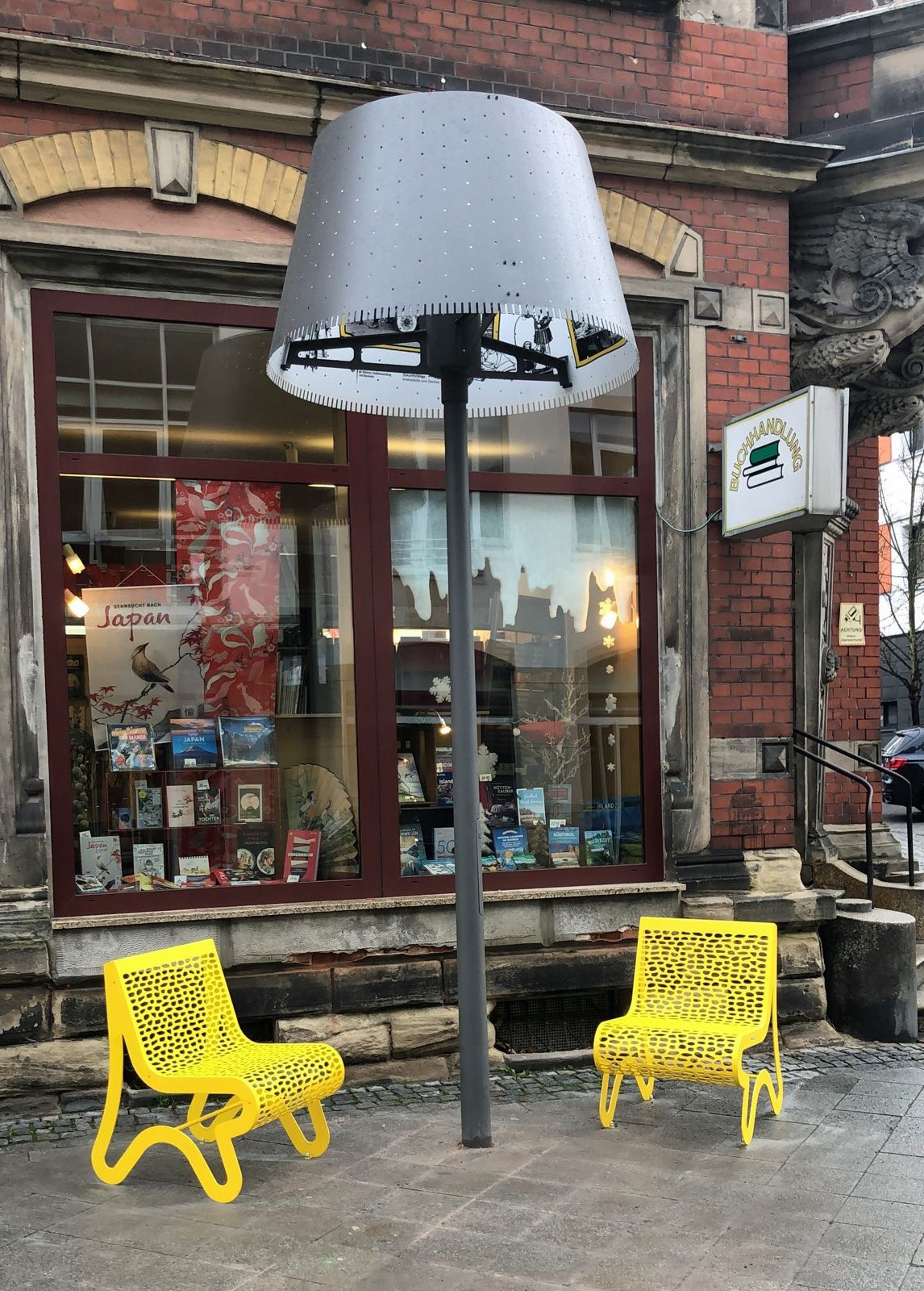 Zwei gelbe Sessel und eine geschosshohe Lampe stehen vor einem Schaufenster.