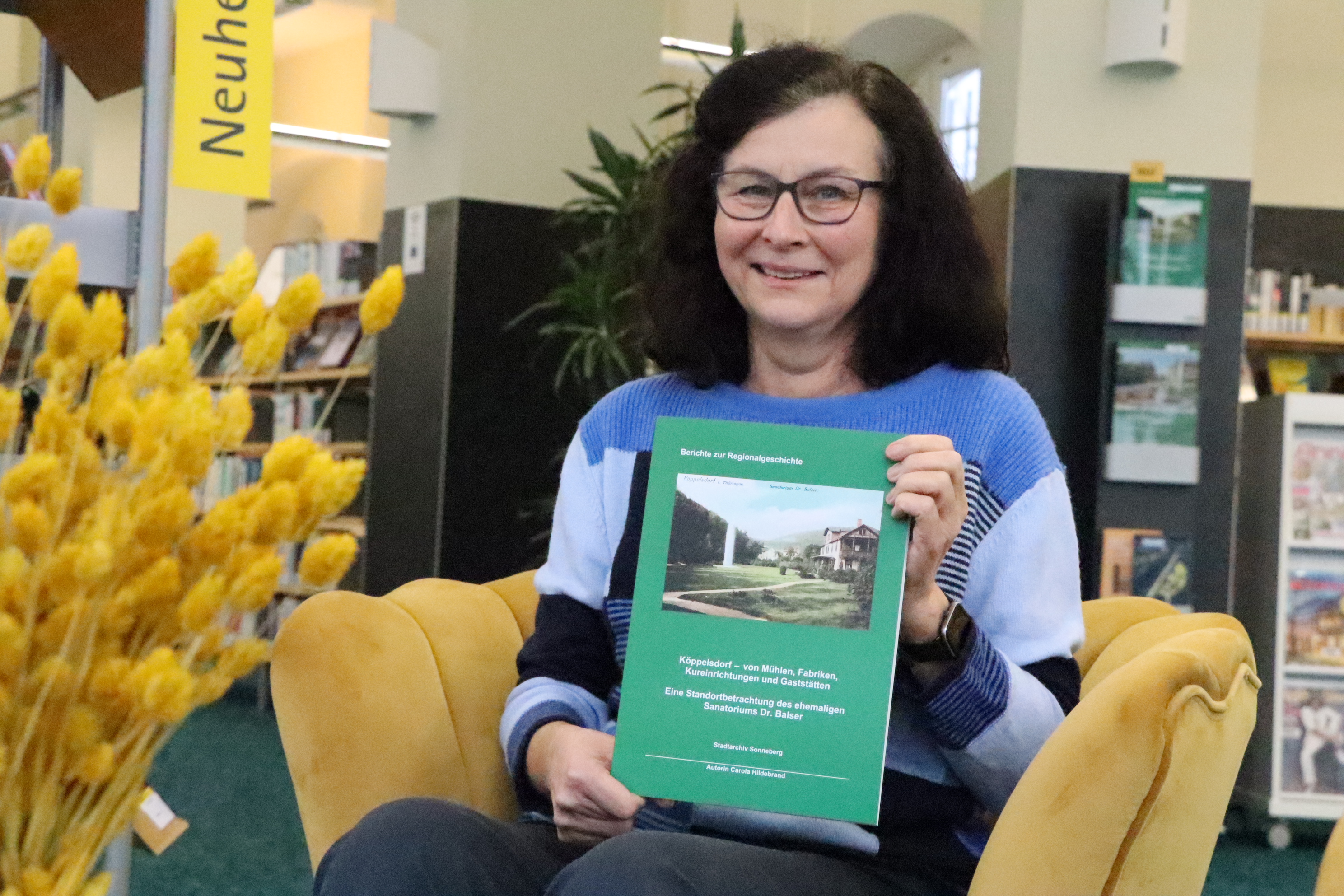 Eine Frau sitzt auf einem Sessel und hält eine A4-große Publikation in die Kamera.