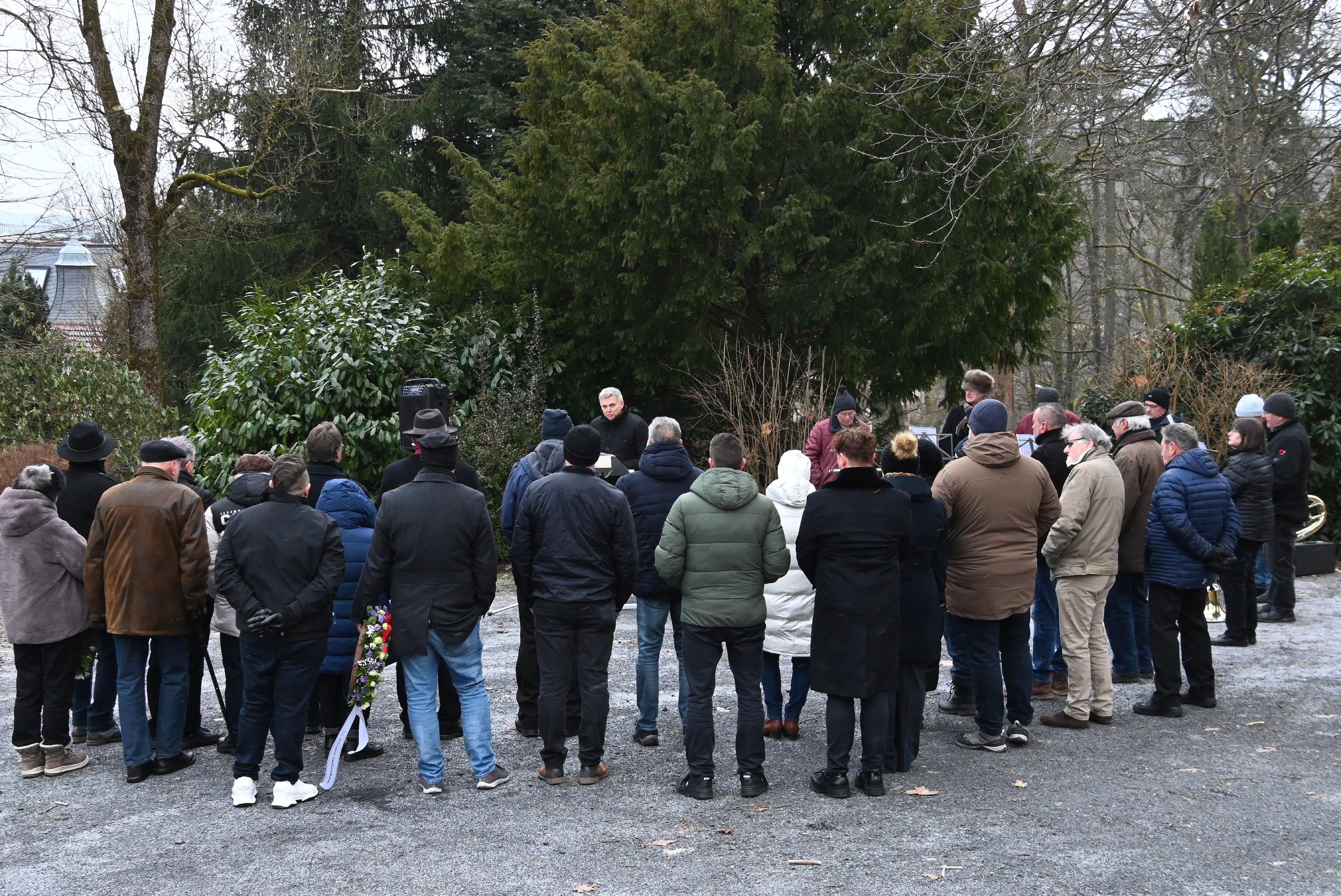 Menschen stehen mit dem Rücken in einem Halbkreis auf einem Friedhof.