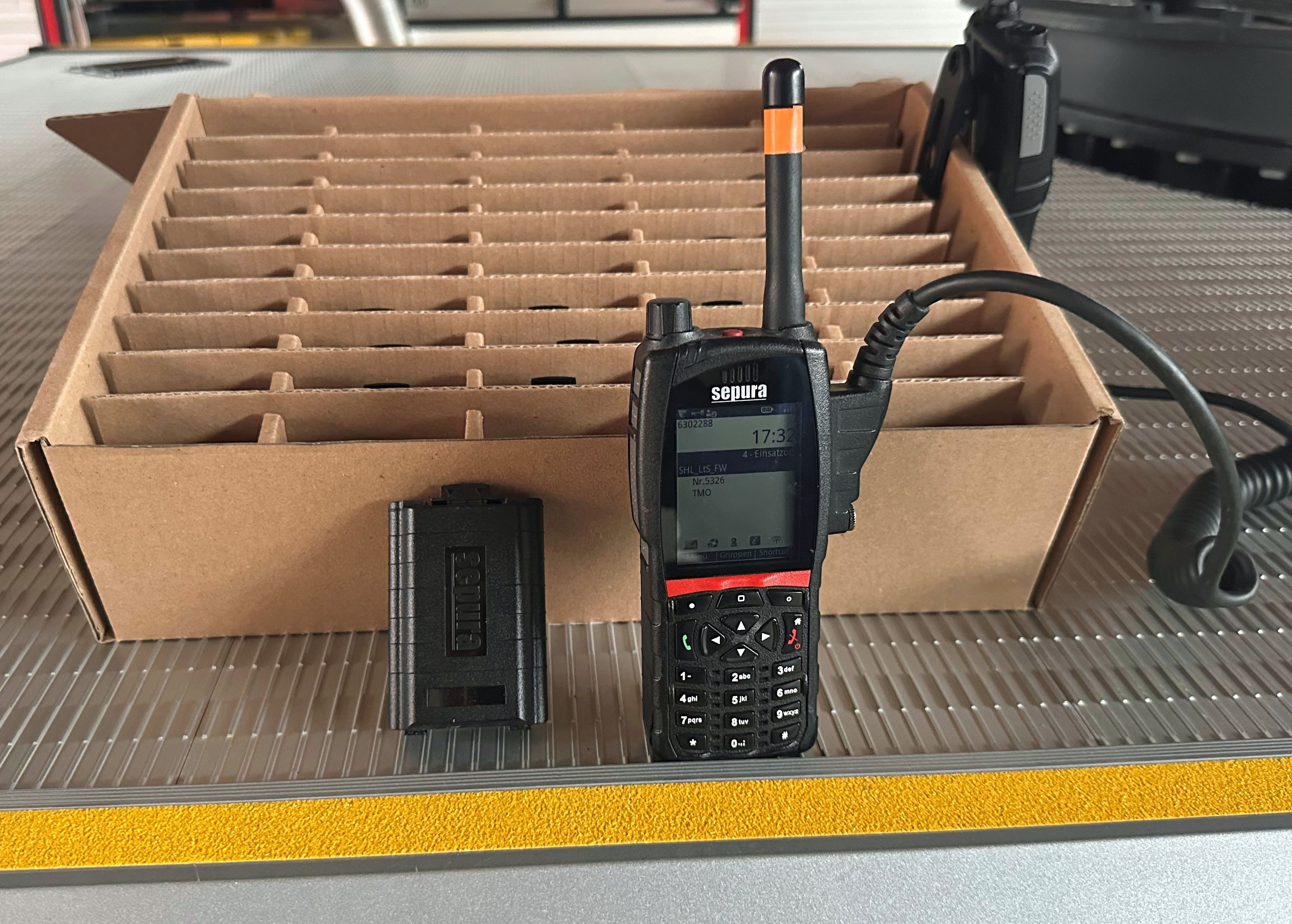 Ein Funksprechgerät und ein Akku dazu stehen vor einem Karton in der Feuerwehr Sonneberg-Mitte.