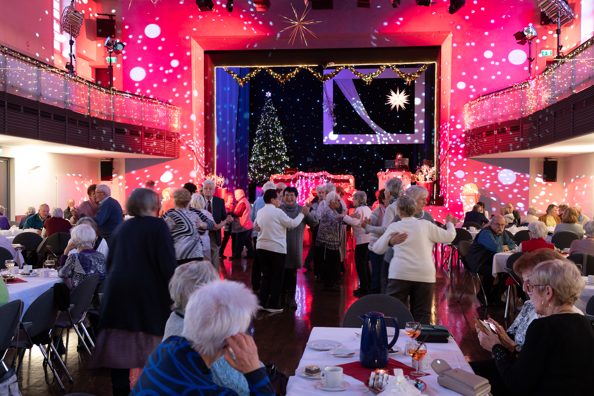 Tanzende Senioren in einem weihnachtlich geschmückten Saal mit Bühne.