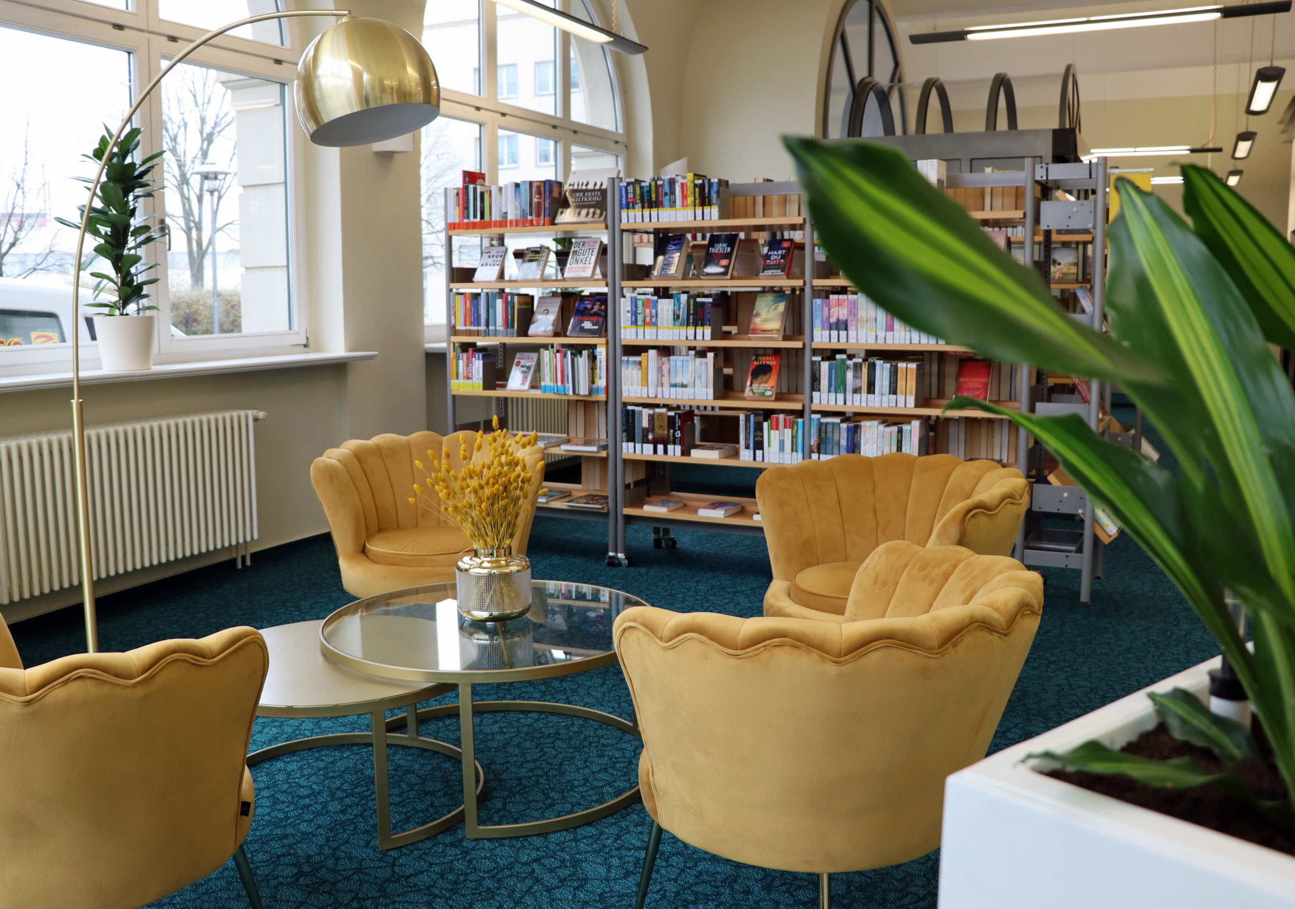 Vier gelbe Sessel stehen um einen Glastisch herum, im Hintergrund stehen Bücherregale der Stadtbibliothek Sonneberg. Gezeigt wird der seit 2024 erneuerte Aufenthaltsbereich.