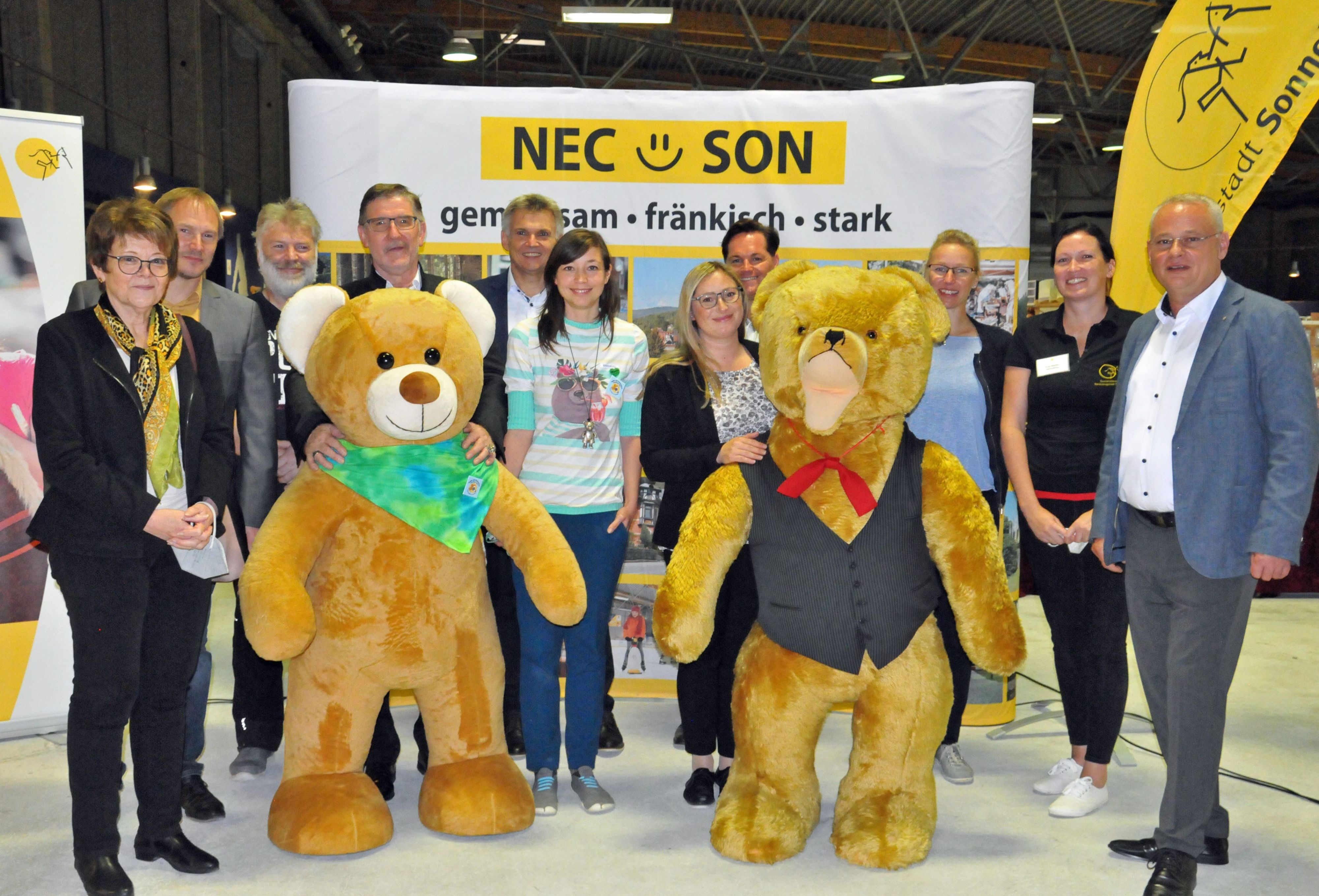 Mehrere Personen stehen mit zwei lebensgroßen Teddybären in einer Reihe.