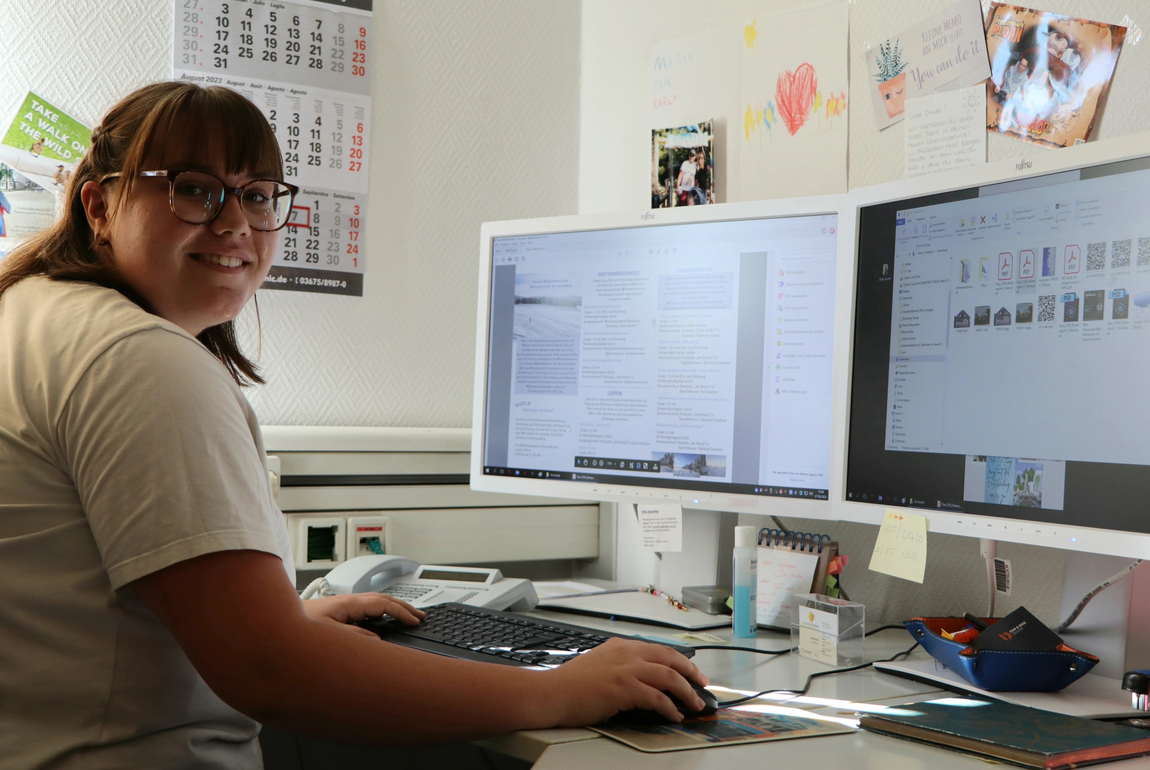 Eine junge Frau sitzt an einem Schreibtisch mit zwei Monitoren.